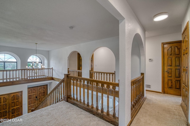 hall with a textured ceiling, light carpet, and a chandelier