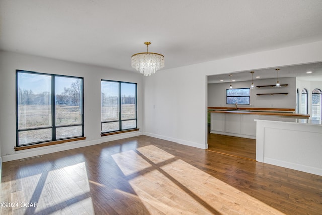 unfurnished living room with a chandelier, hardwood / wood-style floors, a healthy amount of sunlight, and sink