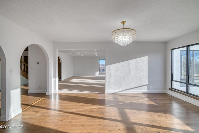 unfurnished room featuring a chandelier, dark wood-type flooring, and a textured ceiling