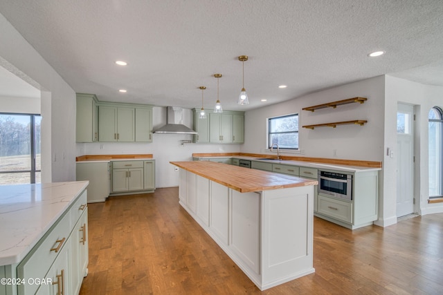 kitchen with wall chimney exhaust hood, light hardwood / wood-style floors, a center island, butcher block countertops, and oven