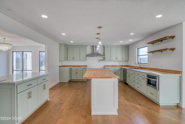 kitchen featuring pendant lighting, wood counters, a center island, wall chimney exhaust hood, and light wood-type flooring