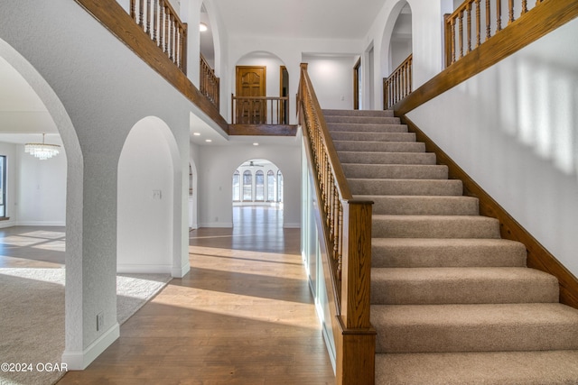 stairs with hardwood / wood-style flooring, a notable chandelier, and a high ceiling