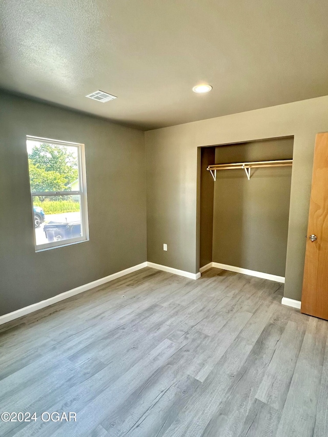 unfurnished bedroom with a closet, a textured ceiling, and light wood-type flooring