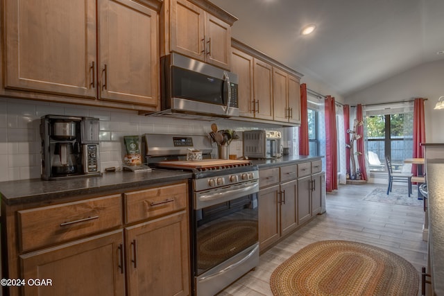 kitchen with light hardwood / wood-style floors, stainless steel appliances, decorative backsplash, and vaulted ceiling