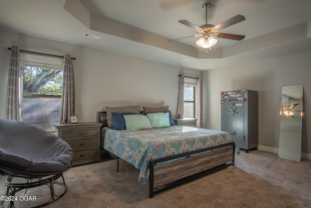 carpeted bedroom featuring ceiling fan, a raised ceiling, and multiple windows