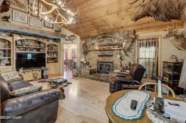 living room with a stone fireplace, light hardwood / wood-style flooring, vaulted ceiling, an inviting chandelier, and built in shelves