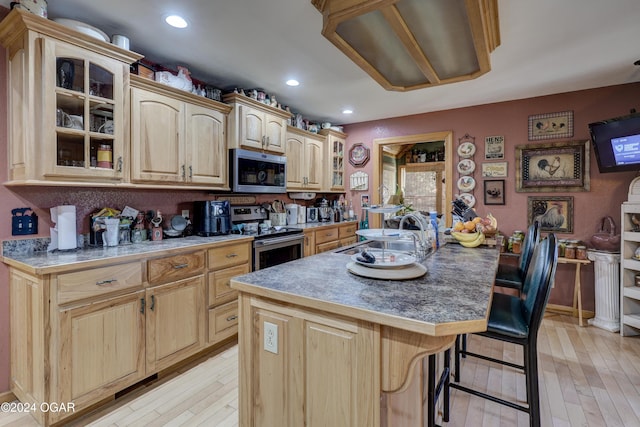 kitchen featuring a breakfast bar area, stainless steel appliances, a center island with sink, sink, and light wood-type flooring