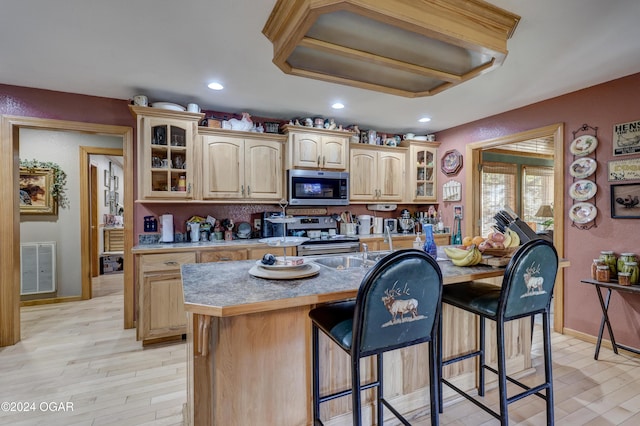 kitchen featuring light brown cabinets, a kitchen breakfast bar, light hardwood / wood-style flooring, stainless steel appliances, and a center island