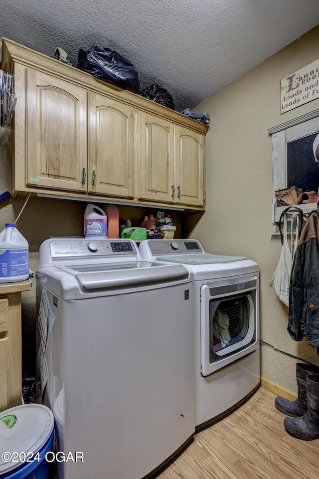 clothes washing area featuring washer and clothes dryer, a textured ceiling, light hardwood / wood-style floors, and cabinets