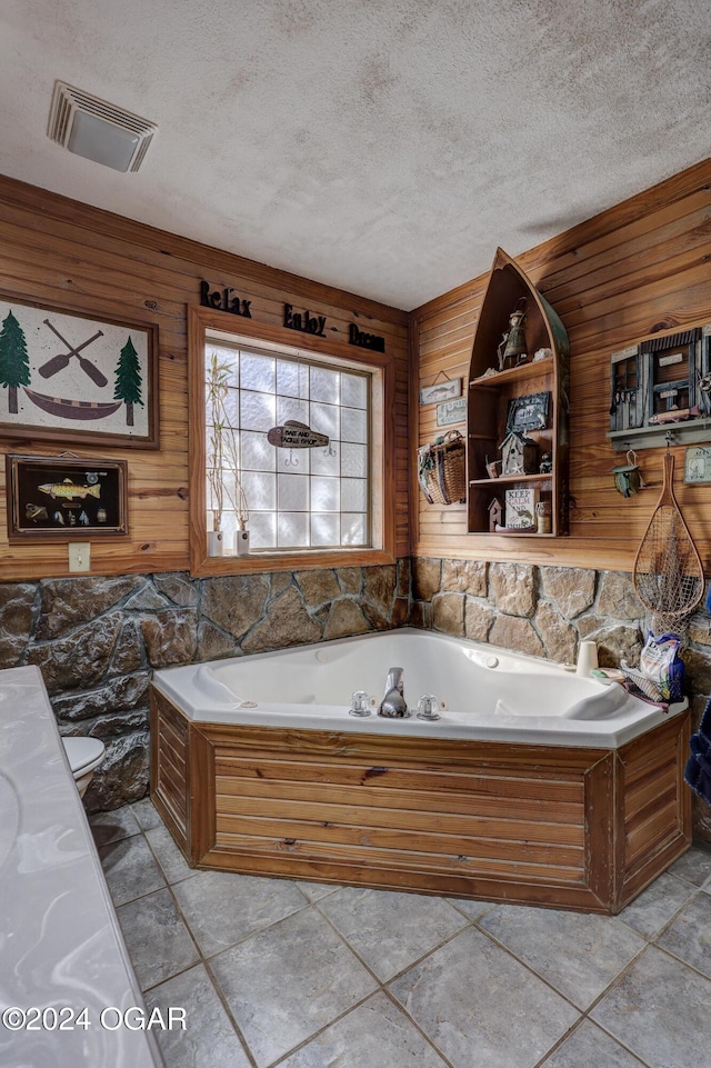 bathroom with a tub, a textured ceiling, and wooden walls