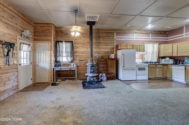 kitchen featuring white appliances, light brown cabinetry, a wood stove, and pendant lighting