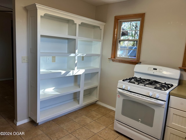 kitchen with light tile patterned flooring, white cabinetry, and gas range gas stove