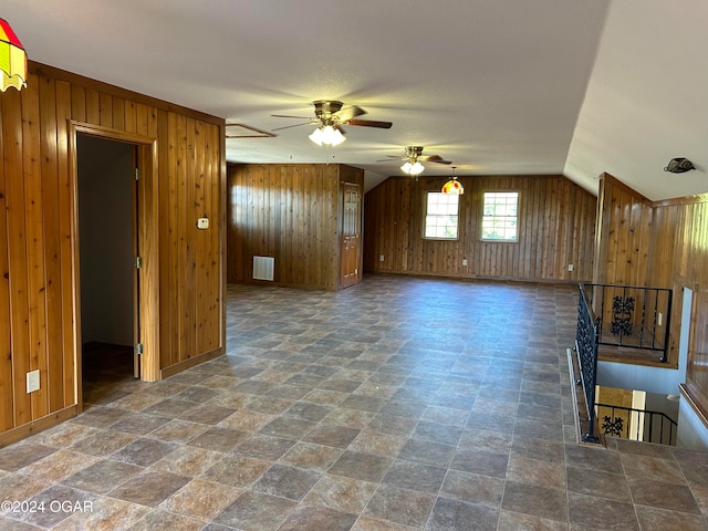 unfurnished living room featuring ceiling fan, wood walls, and vaulted ceiling