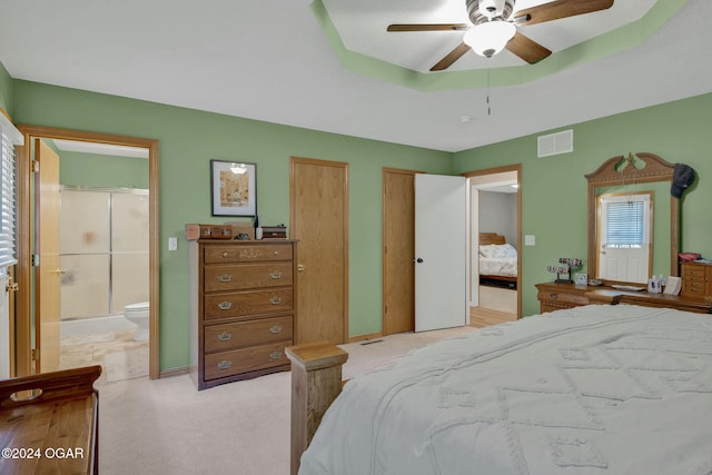 bedroom with connected bathroom, light carpet, a raised ceiling, two closets, and ceiling fan