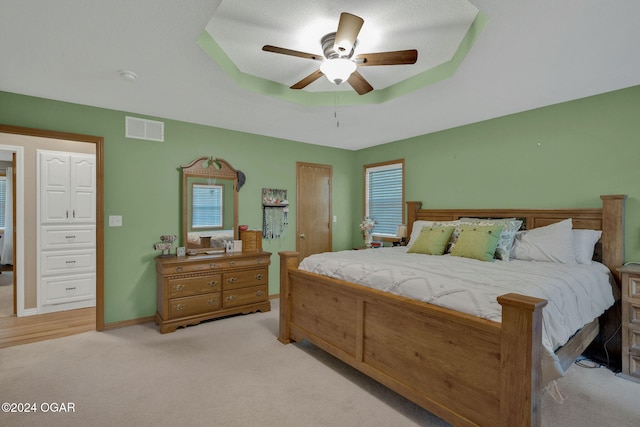 carpeted bedroom with a raised ceiling and ceiling fan