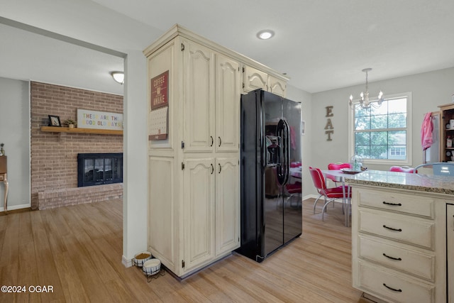 kitchen with a brick fireplace, pendant lighting, light hardwood / wood-style floors, and black fridge with ice dispenser