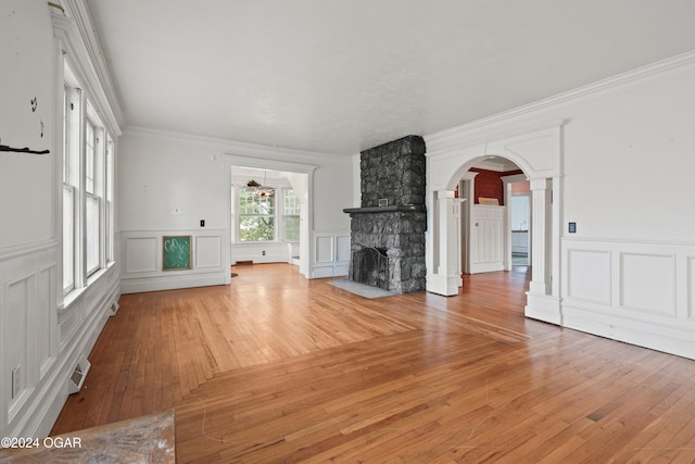 unfurnished living room featuring hardwood / wood-style flooring, ornamental molding, and a stone fireplace