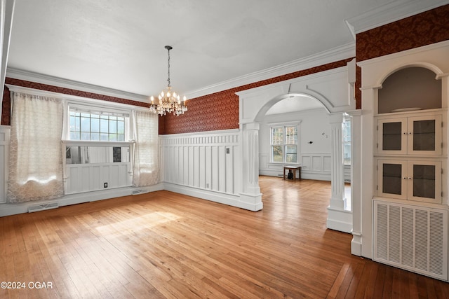 unfurnished dining area featuring decorative columns, a notable chandelier, and wood-type flooring