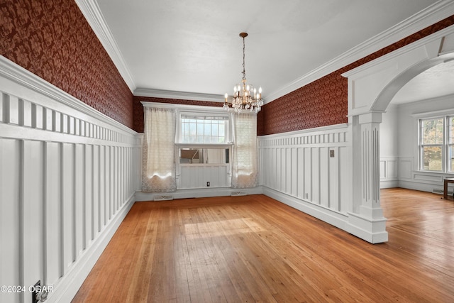 unfurnished dining area featuring light hardwood / wood-style floors, crown molding, decorative columns, and an inviting chandelier