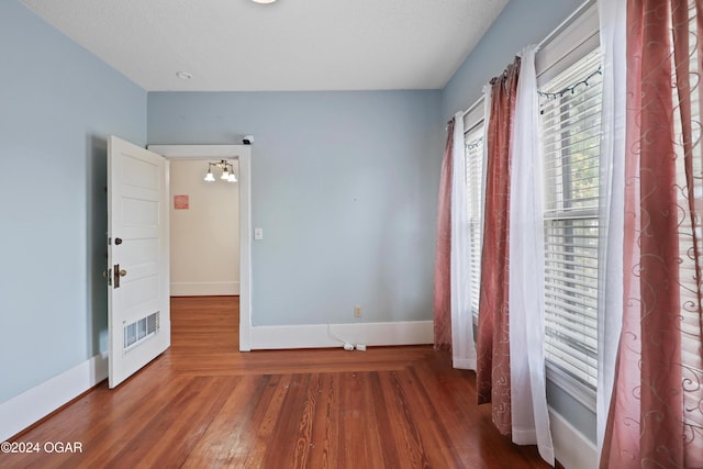 unfurnished bedroom featuring a chandelier, a textured ceiling, and dark hardwood / wood-style flooring