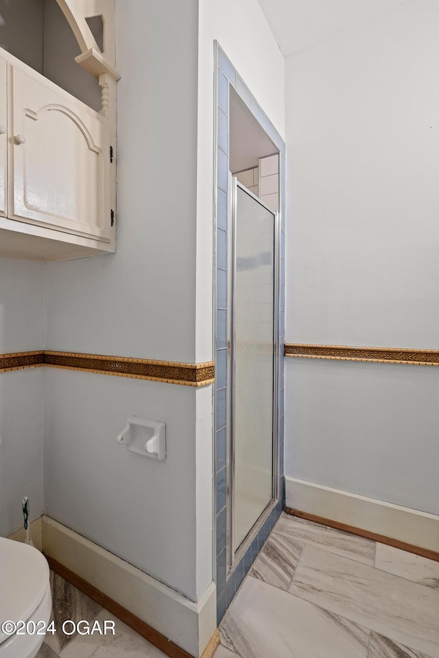 bathroom featuring a shower with door and toilet