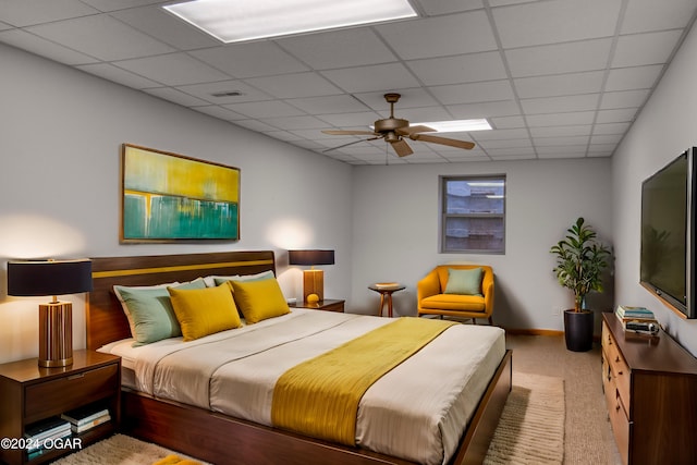 bedroom with a drop ceiling, light colored carpet, and ceiling fan