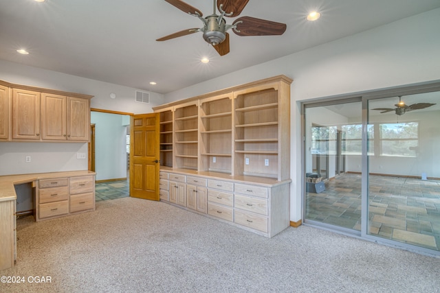 unfurnished office with built in desk, light colored carpet, and ceiling fan