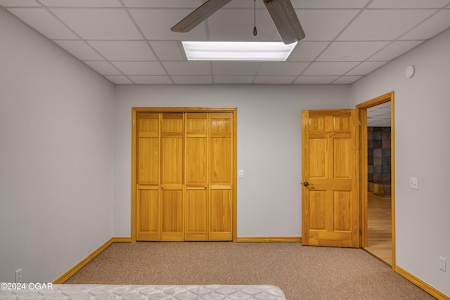 unfurnished bedroom with carpet flooring, a drop ceiling, ceiling fan, and a closet