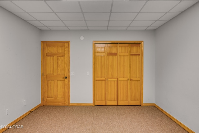 unfurnished bedroom featuring a drop ceiling, light carpet, and a closet