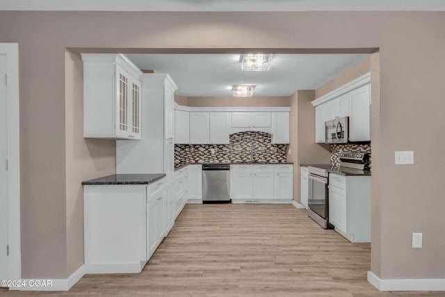 kitchen with appliances with stainless steel finishes, backsplash, white cabinets, dark stone countertops, and light hardwood / wood-style flooring