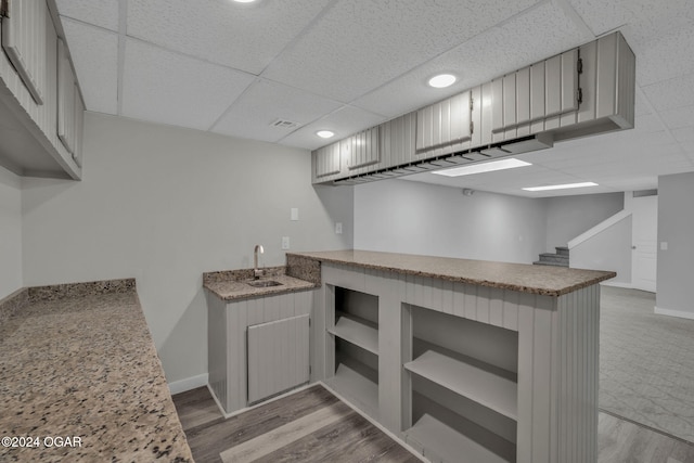 kitchen with light hardwood / wood-style floors, a drop ceiling, sink, and kitchen peninsula