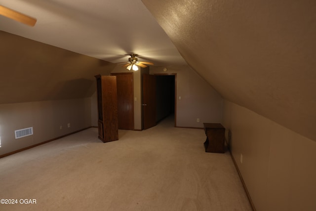 additional living space with a textured ceiling, vaulted ceiling, light colored carpet, and ceiling fan