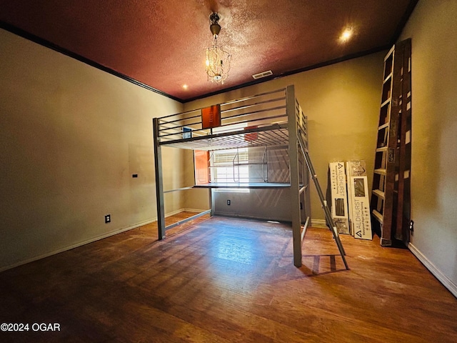 unfurnished bedroom featuring wood-type flooring, a textured ceiling, an inviting chandelier, and crown molding