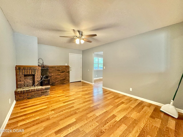 living room featuring light hardwood / wood-style floors, a textured ceiling, a brick fireplace, and ceiling fan