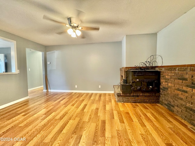 unfurnished living room with light hardwood / wood-style flooring, a brick fireplace, a textured ceiling, and ceiling fan