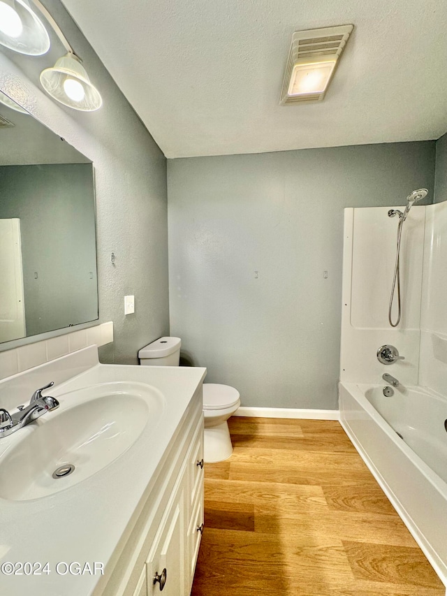 full bathroom featuring hardwood / wood-style floors, a textured ceiling, toilet, vanity, and washtub / shower combination