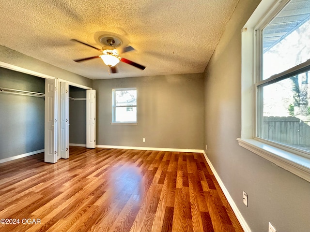 unfurnished bedroom with ceiling fan, wood-type flooring, a textured ceiling, and two closets