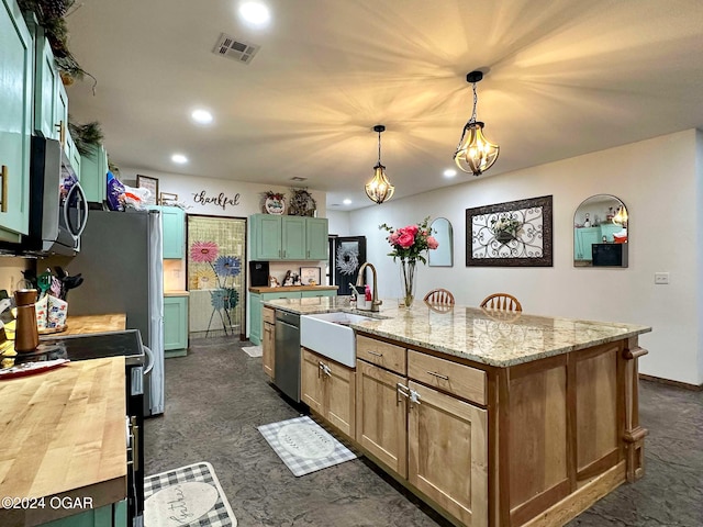 kitchen with an island with sink, appliances with stainless steel finishes, decorative light fixtures, light stone counters, and sink