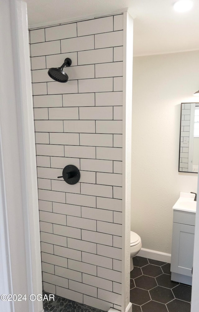 bathroom featuring vanity, a tile shower, toilet, and tile patterned flooring