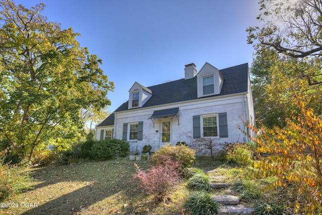 cape cod-style house featuring brick siding, a chimney, a front lawn, and roof with shingles