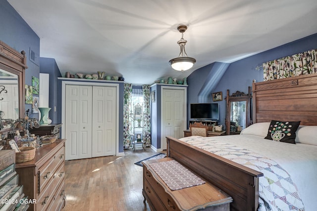 bedroom with lofted ceiling, multiple closets, and light wood-style floors