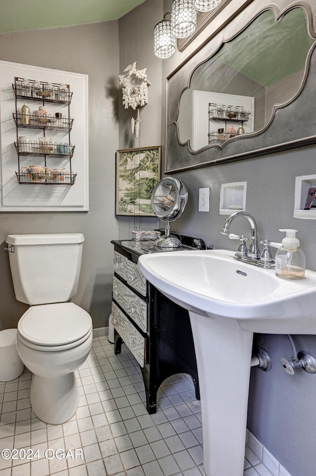 half bathroom featuring lofted ceiling, toilet, a sink, baseboards, and tile patterned floors