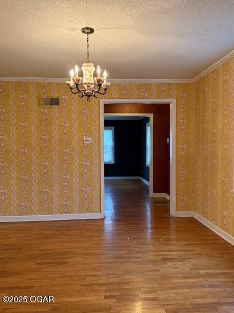 unfurnished dining area with wallpapered walls, baseboards, wood finished floors, a textured ceiling, and crown molding