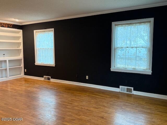 empty room with ornamental molding, wood finished floors, visible vents, and baseboards