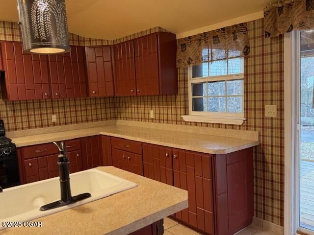 kitchen featuring wallpapered walls, decorative backsplash, light countertops, black range oven, and a sink