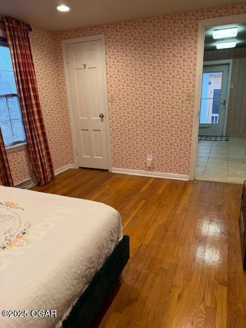 bedroom featuring wood finished floors, baseboards, and wallpapered walls