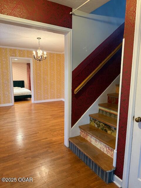 stairs featuring crown molding, wood finished floors, a chandelier, baseboards, and wallpapered walls