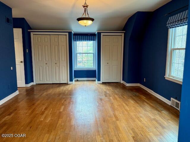 unfurnished bedroom featuring light wood-style floors, baseboards, visible vents, and multiple closets