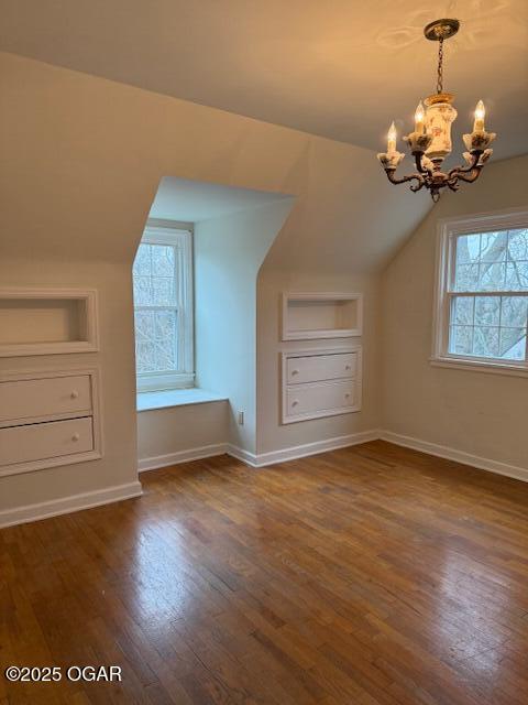 additional living space featuring vaulted ceiling, an inviting chandelier, dark wood finished floors, and baseboards