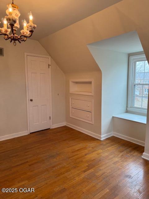 bonus room featuring dark wood-type flooring, lofted ceiling, a chandelier, and baseboards